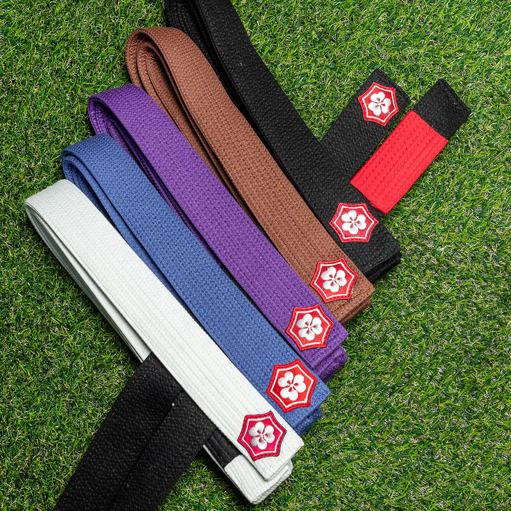 KANJI KAZE BJJ belts in five colors with a red-bar black belt on training turf
