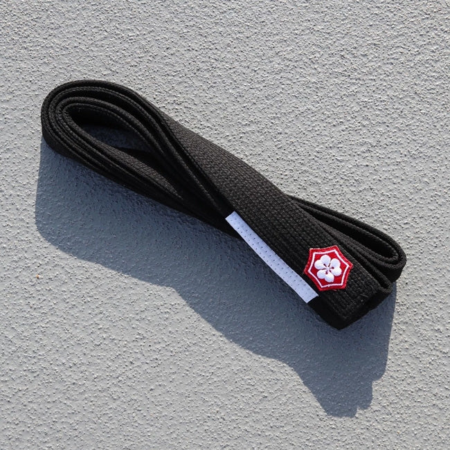 Black KANJI KAZE BJJ belt with a white rank bar folded on concrete