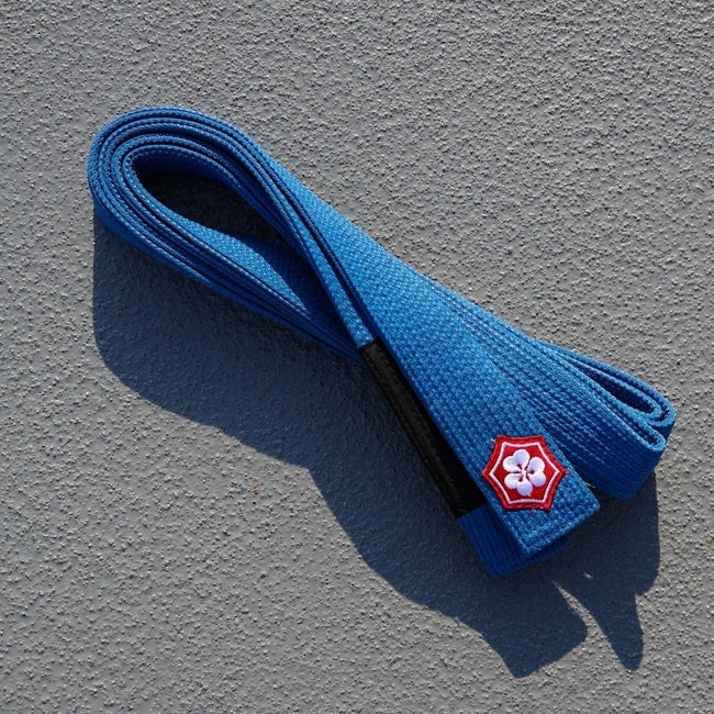 Blue KANJI KAZE BJJ belt with a black rank bar folded on concrete
